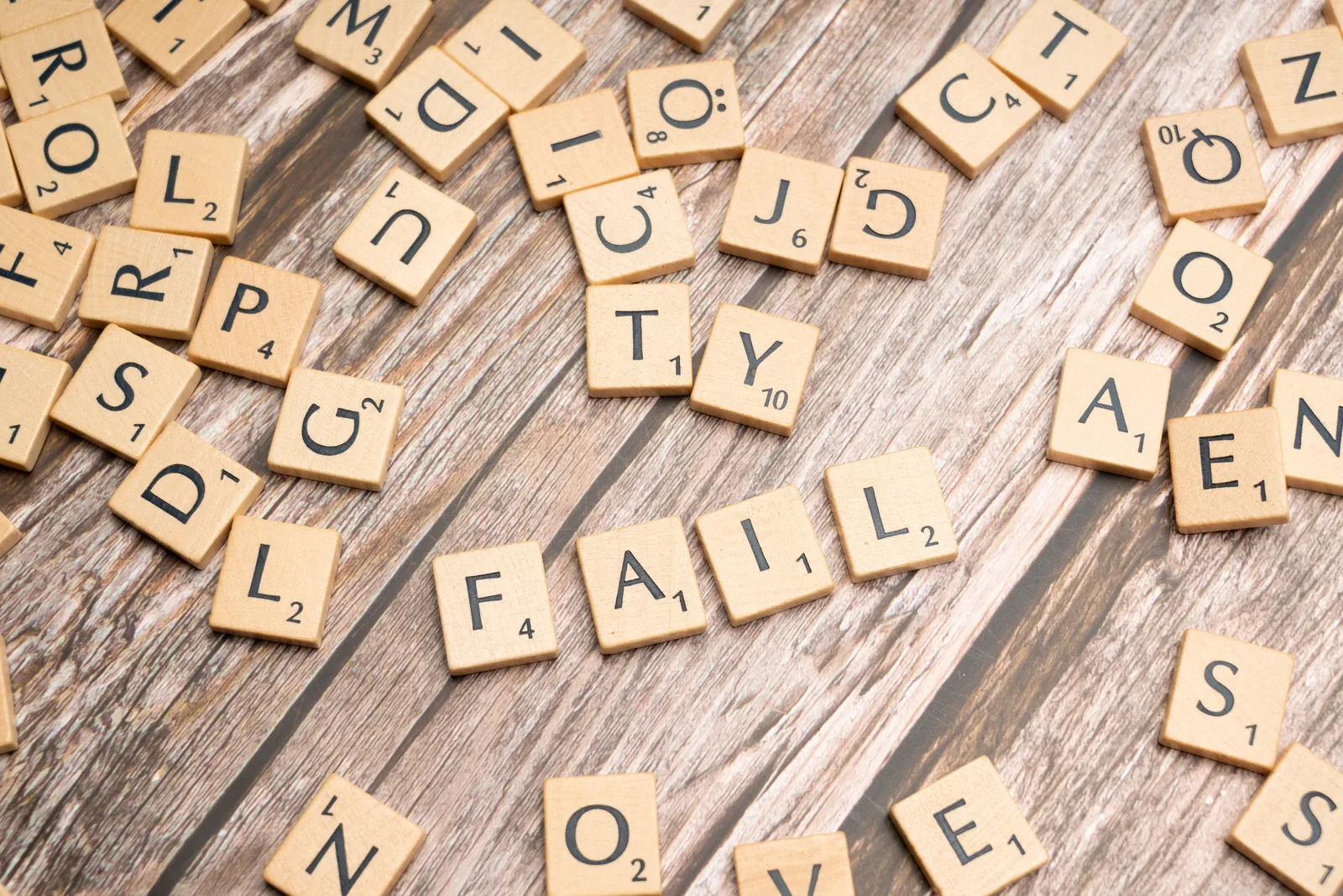 Scrabble tiles on wood form 'FAIL', symbolizing defeat and reflection.